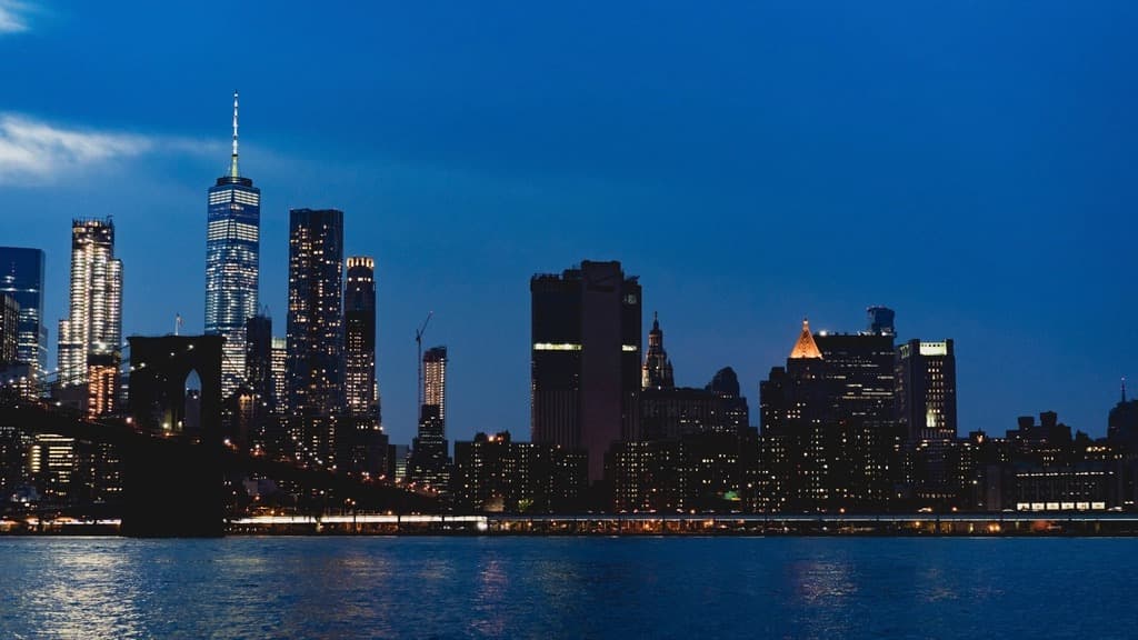 Lower Manhattan skyline lit up at night seen across the East River with the Brooklyn Bridge
