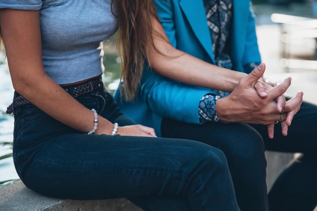 Two people seated side by side outdoors, one in a blue blazer, hands resting in their laps