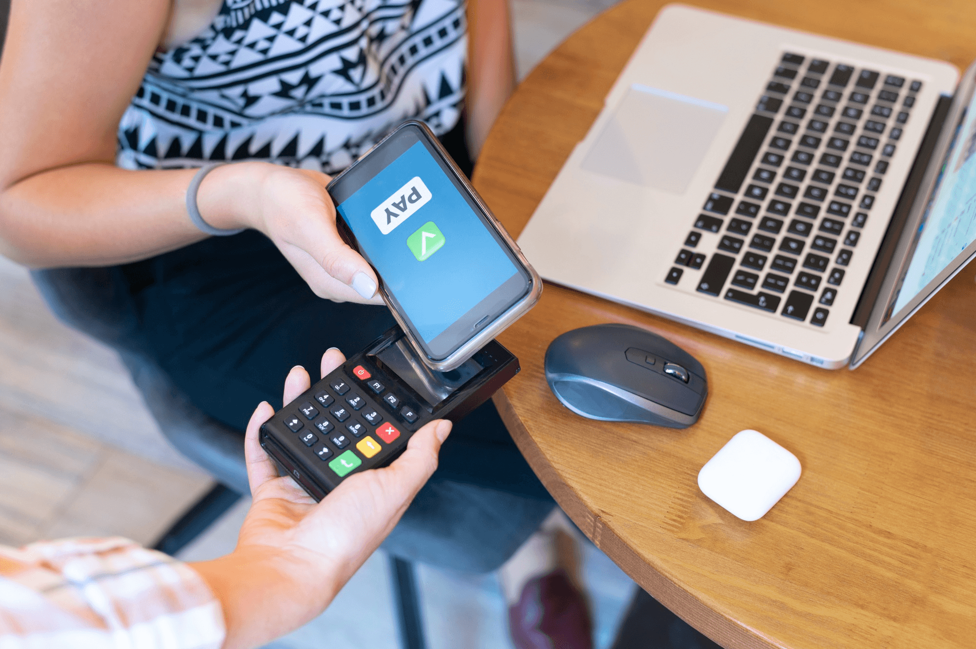A person paying with a smartphone wallet app on a card payment terminal beside a laptop