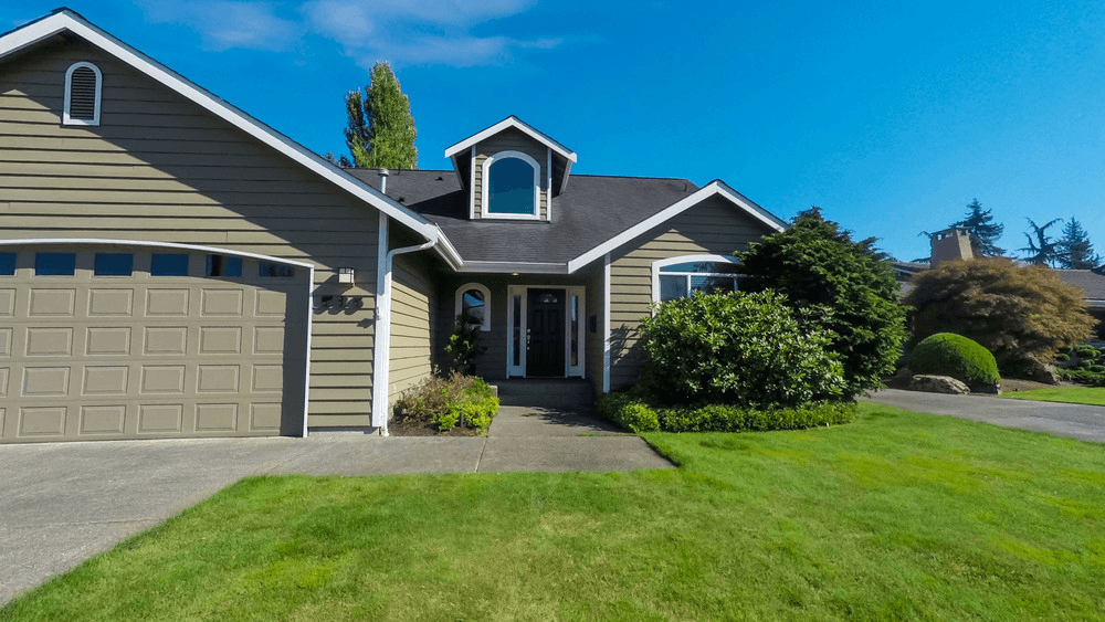 A single-family suburban house with a shingled roof, green lawn, and clear blue sky