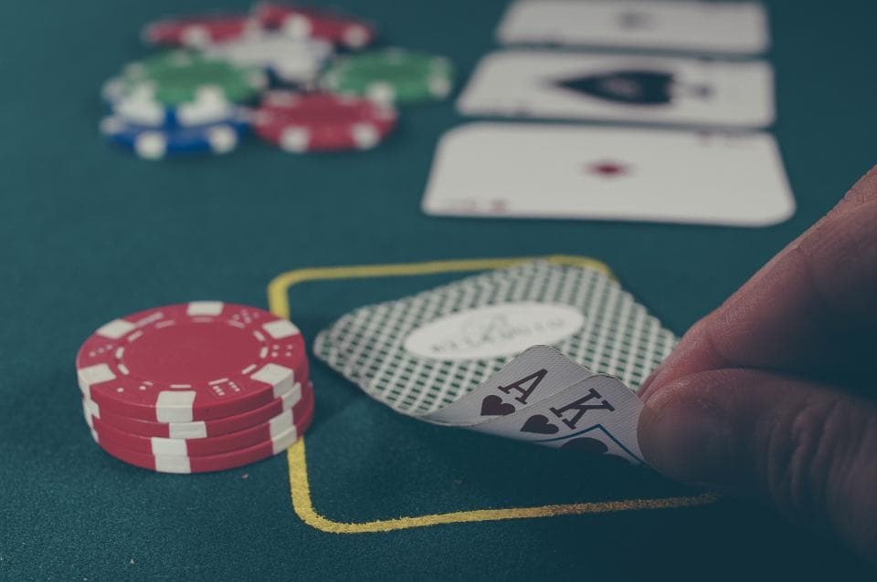 Player peeking at ace and king hole cards on a green poker table beside stacks of chips