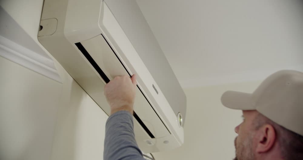 HVAC technician servicing a wall-mounted air conditioning unit in a home
