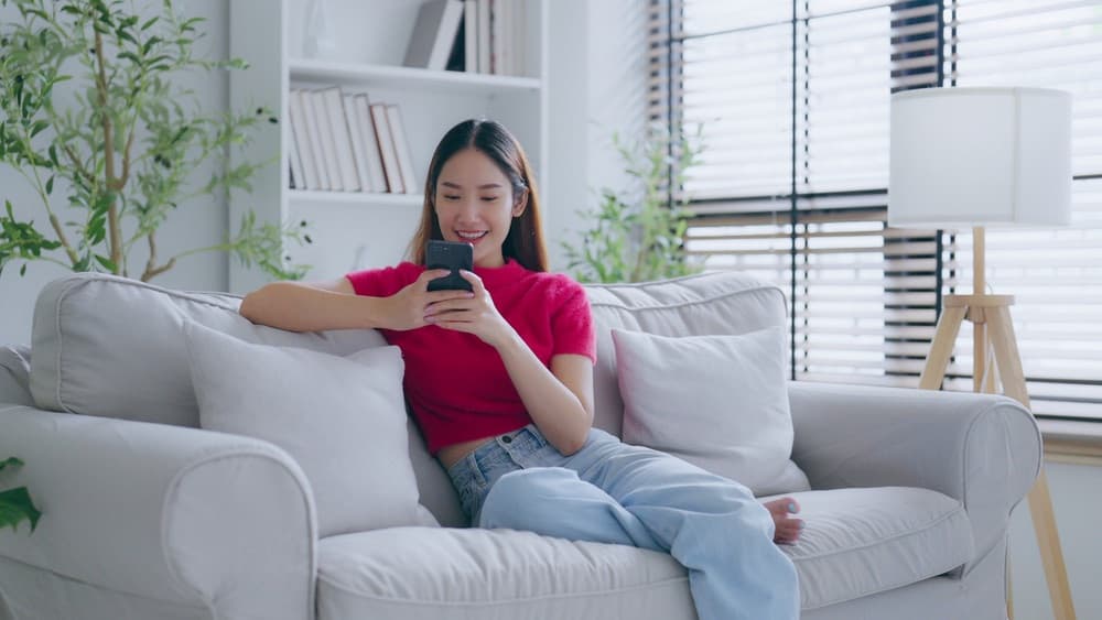 Woman relaxing on a sofa in a bright living room using her phone