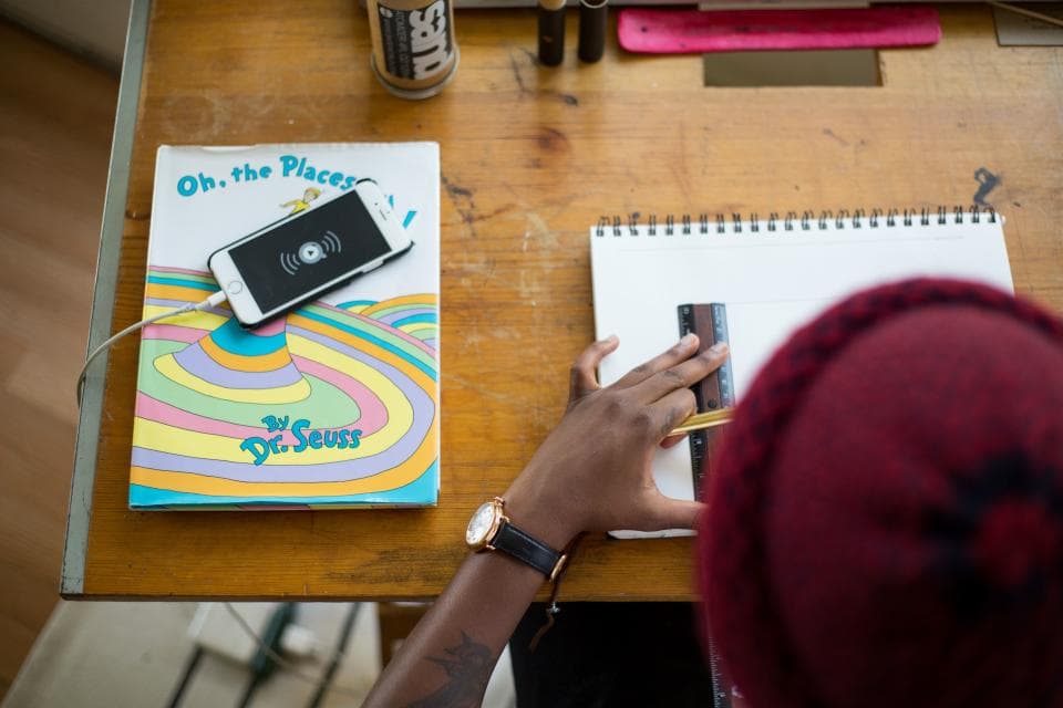 Student at a desk working in a notebook with a smartphone resting on a book