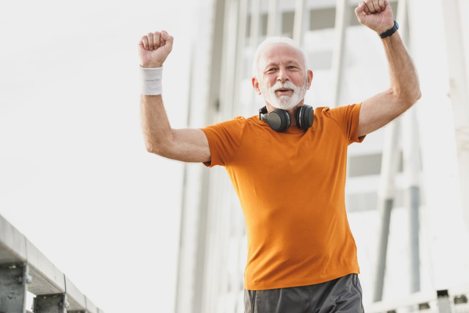 Older man in an orange shirt raising his arms in celebration after exercising outdoors