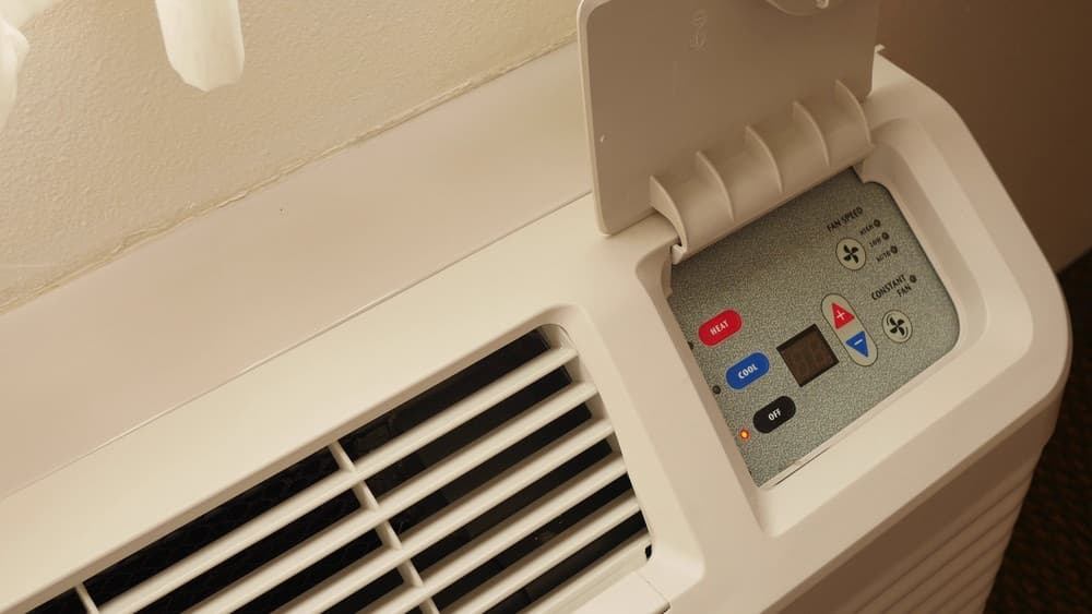 Control panel of an aging through-the-wall HVAC unit with heat, cool and fan speed buttons