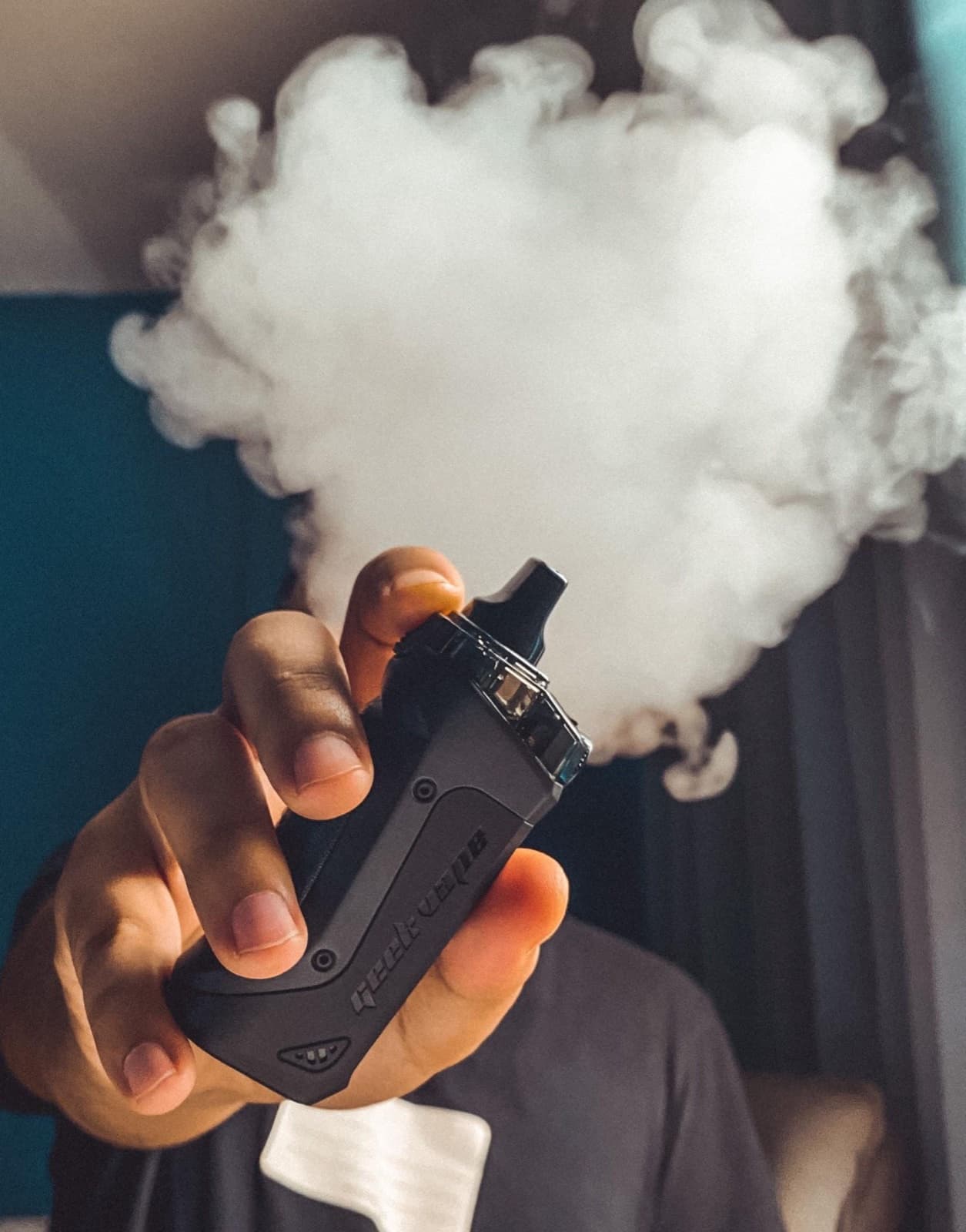 Hand holding a black vape device with a cloud of vapor