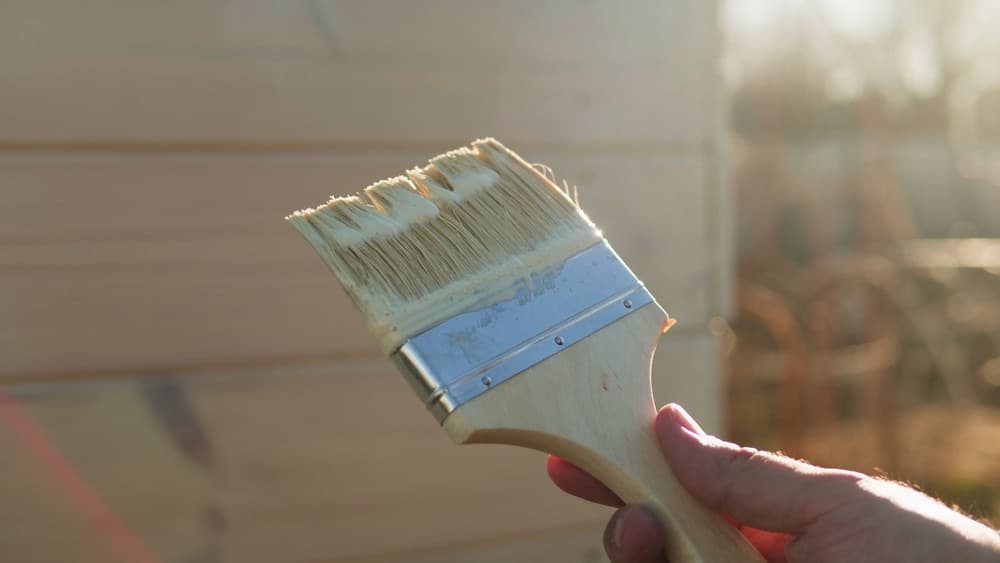 Paintbrush with fresh paint in front of a house exterior