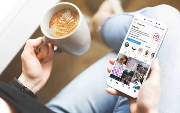 Hand holding a phone showing an Instagram profile next to a cup of coffee