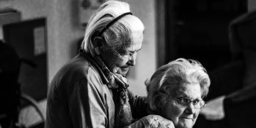 greyscale photo of woman standing behind woman sitting on chair