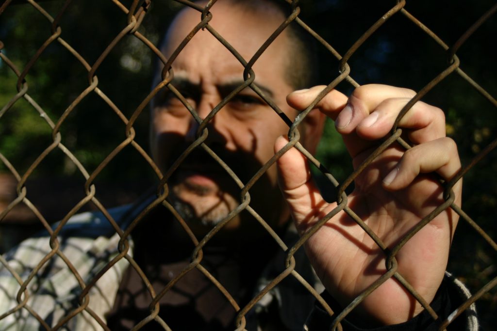 a man behind a chain link fence making a face