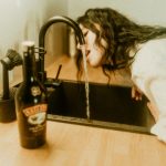 a woman drinking water from a kitchen sink