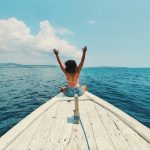 woman wearing blue denim short-shorts sitting on boat raising hands