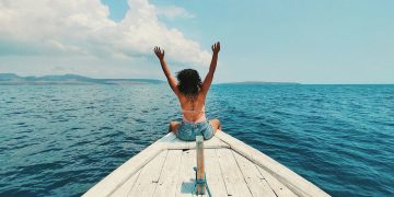 woman wearing blue denim short-shorts sitting on boat raising hands